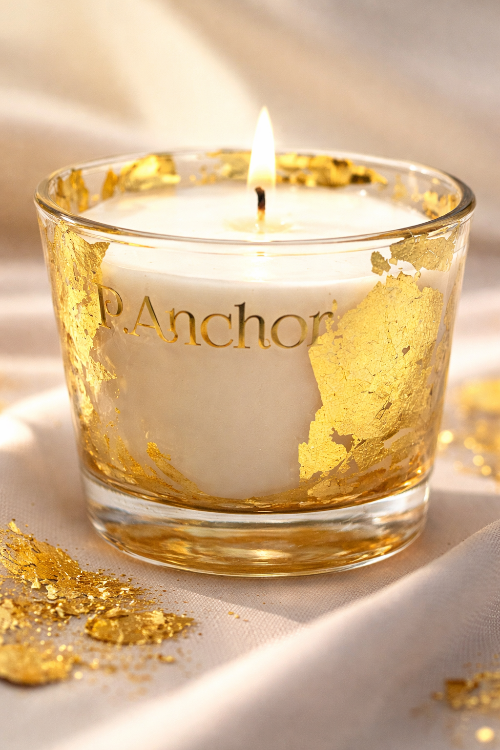 Candle in a glass holder with gold leaf, featuring the brand 'R. Anchora', on a soft background.