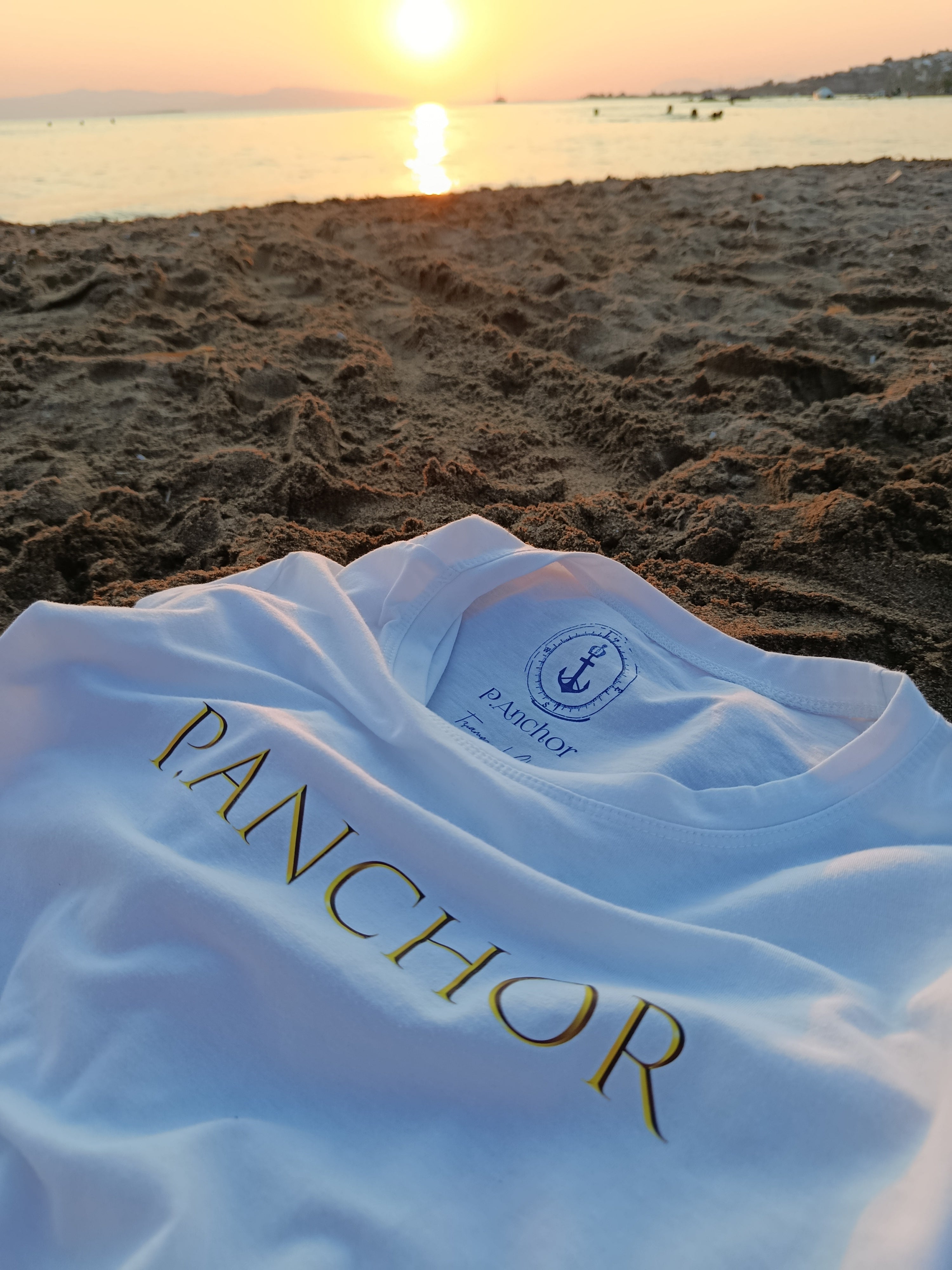 White towel with 'PANCHOR' branding on a sandy beach at sunset