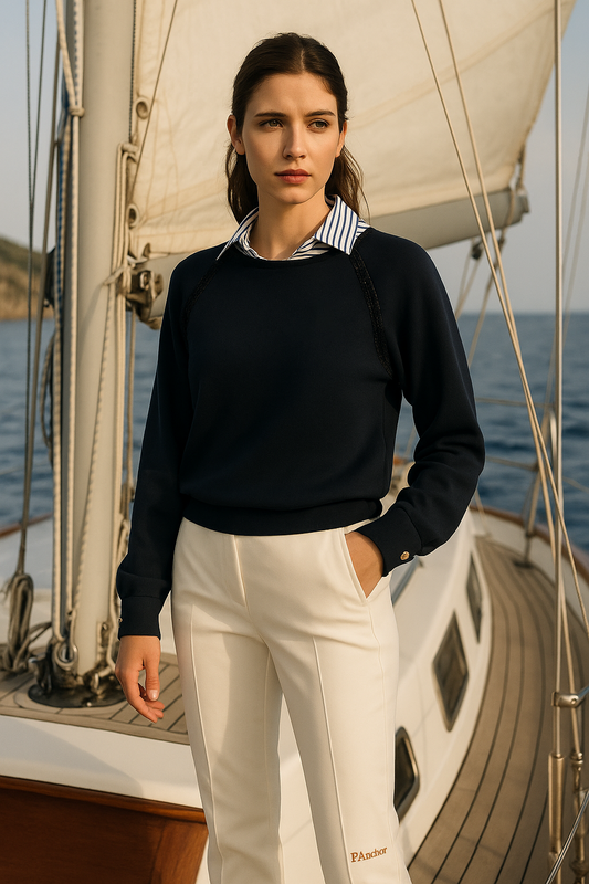 Woman standing on a sailboat wearing a black sweater and white pants.