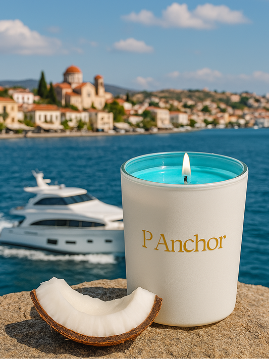 Candle with 'P Anchor' branding on a beach with a coastal town in the background