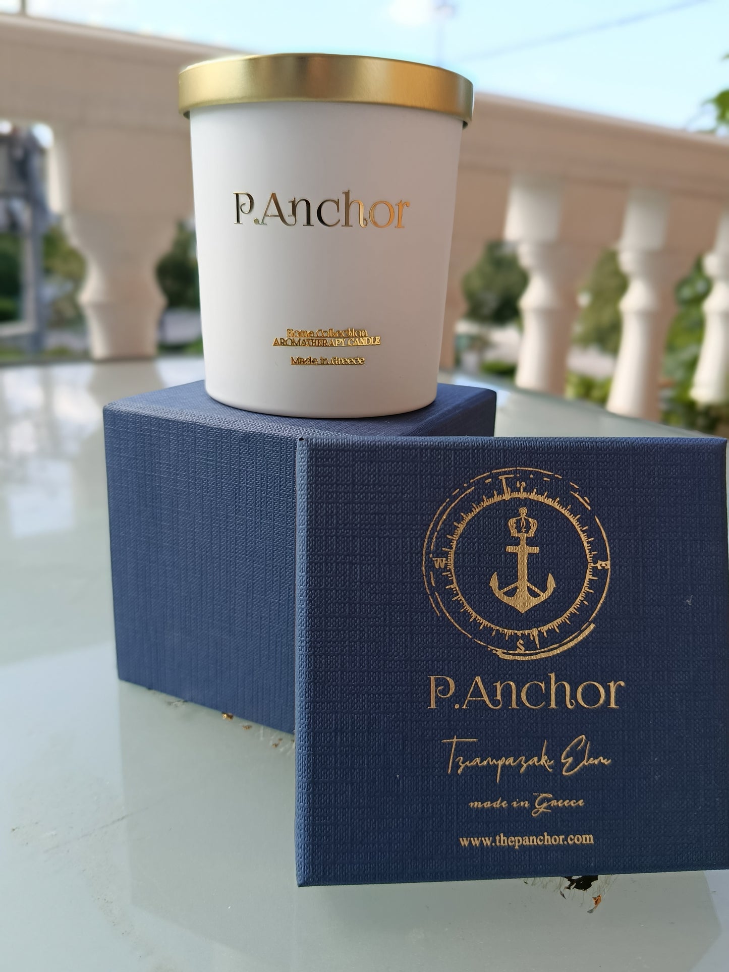 Luxury aromatherapy candle by P.Anchor in white jar with gold lid, displayed on navy blue gift box with gold anchor logo – Made in Greece