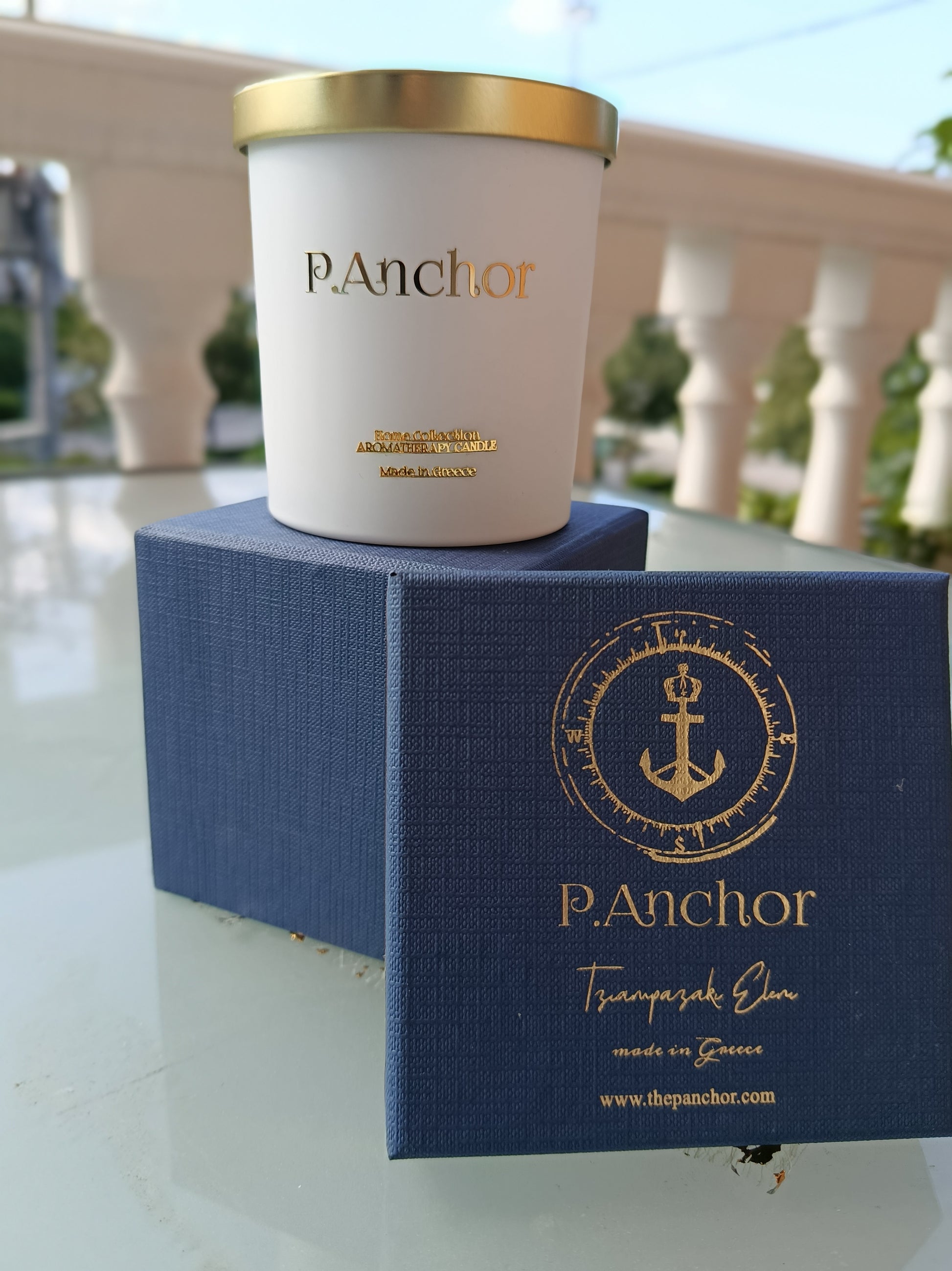 Luxury aromatherapy candle by P.Anchor in white jar with gold lid, displayed on navy blue gift box with gold anchor logo – Made in Greece