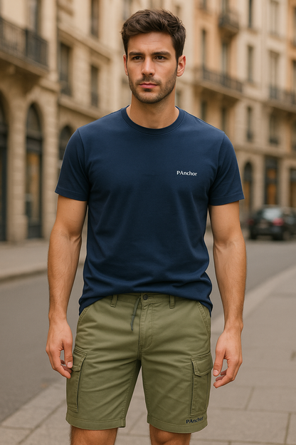 alt="Male model wearing a navy blue P.Anchor t-shirt and sage green cargo shorts, standing confidently in a stylish urban setting, showcasing a casual yet refined summer look"
