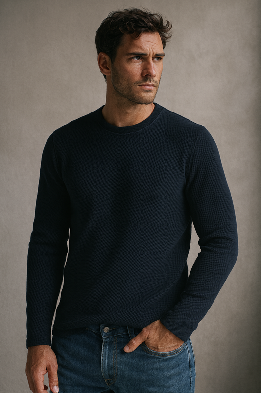 “Male model in navy long-sleeve waffle-knit crewneck and blue jeans, standing against a soft grey wall; close, vertical composition.”