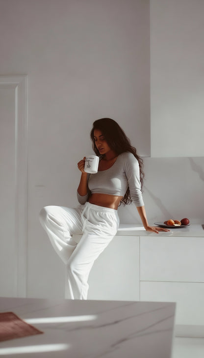 Woman sitting on a white counter holding a mug in a minimalistic kitchen.
