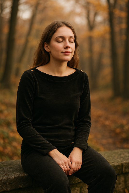 “Woman in black velvet set—boat-neck blouse with shoulder buttons and trousers—sitting with eyes closed in an autumn park